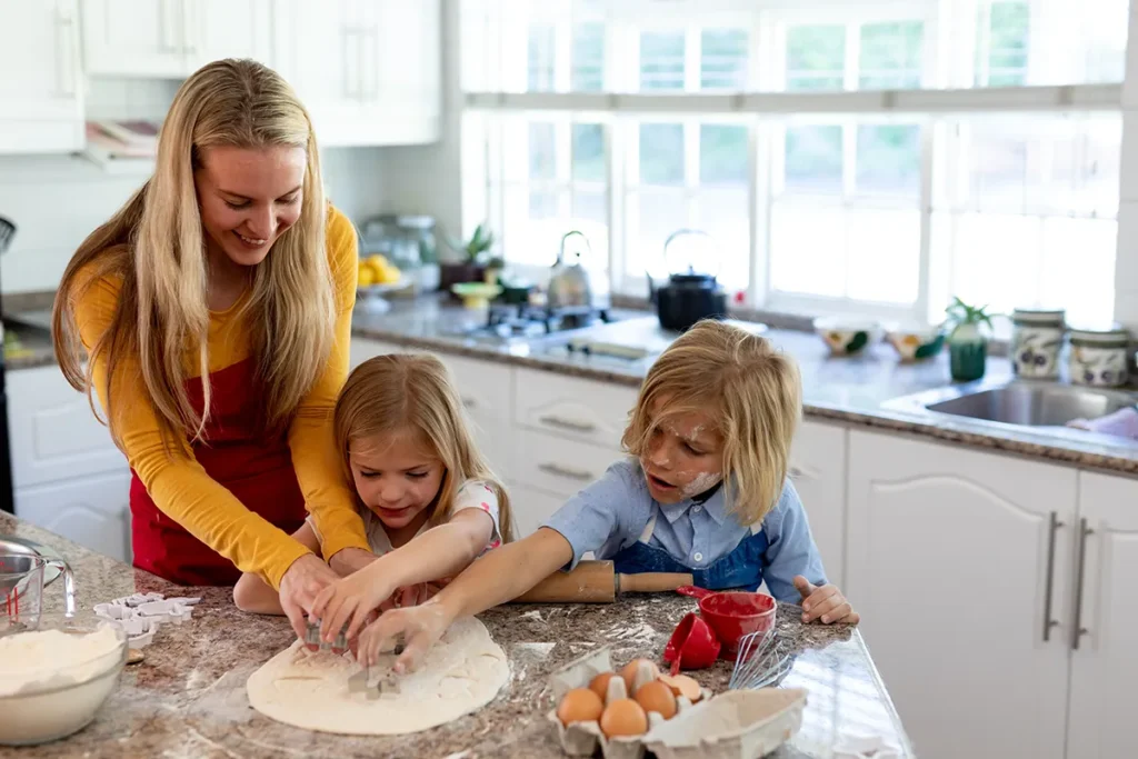 a mom and two kids making holiday cookies in the kitchen