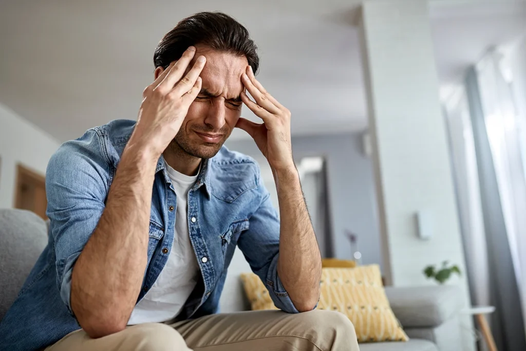 chronic-headaches a man suffering from a headache at home and holding his hands to his head